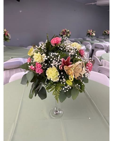 Tall round centerpiece of pink roses, yellow carnations, lilies, and baby's breath in a clear glass vase