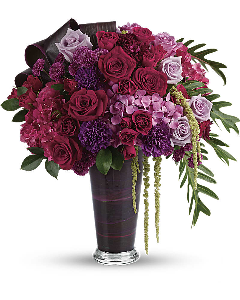 Tall arrangement of red and purple roses, carnations, and hydrangeas in a dark glass vase