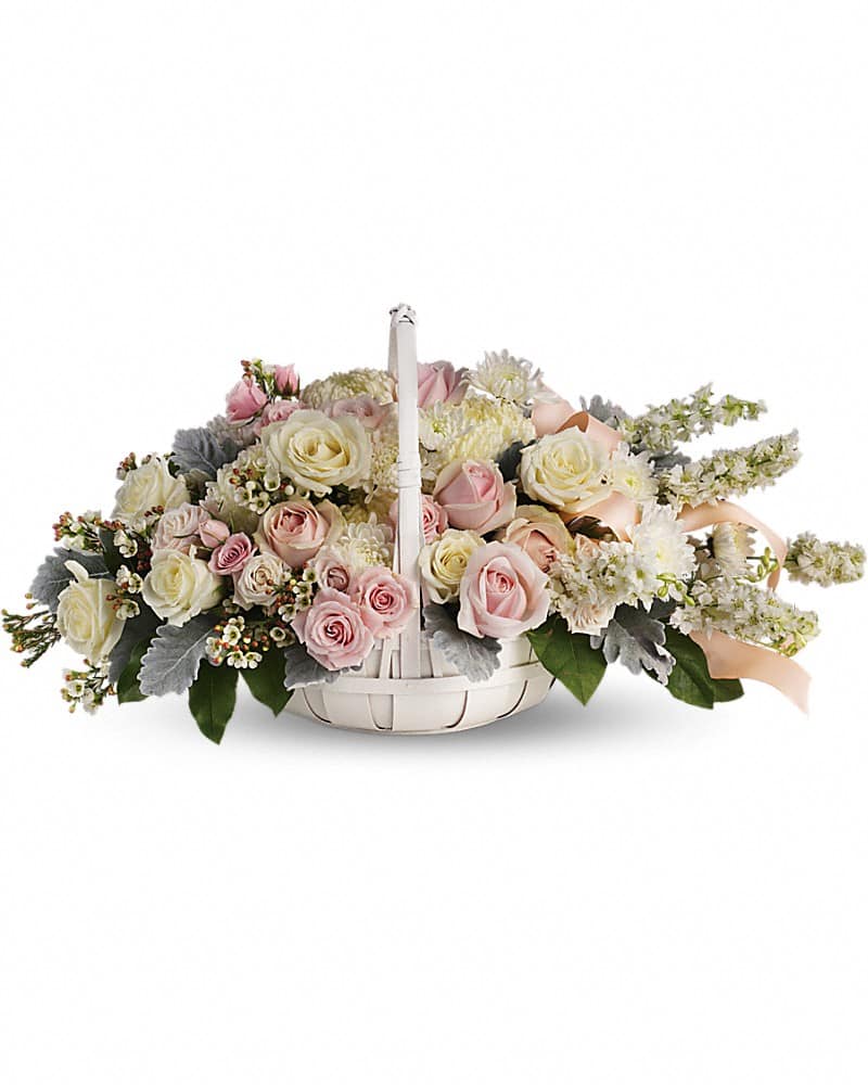 Low white basket of pale pink and cream roses with white flowers and a soft peach ribbon