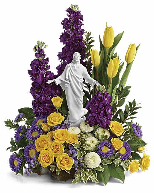 Sacred Grace Bouquet - A reverent and radiant springtime gift, this unique bouquet of yellow roses and tulips, accented with rich purple blooms, surrounds a peaceful porcelain keepsake statue. This graceful bouquet features yellow spray roses, yellow tulips, purple stock, lavender matsumoto asters, white button spray chrysanthemums, lavender sinuata statice, oregonia, myrtle, galax leaves, and lemon leaf. Delivered with Teleflora's Sacred Grace Keepsake. Orientation: One-Sided  SUBSTITUTION POLICY Please note the bouquet pictured reflects our original design.  If the exact flowers or container in this arrangement are not available, our local florists will create a beautiful bouquet with the freshest available flowers.