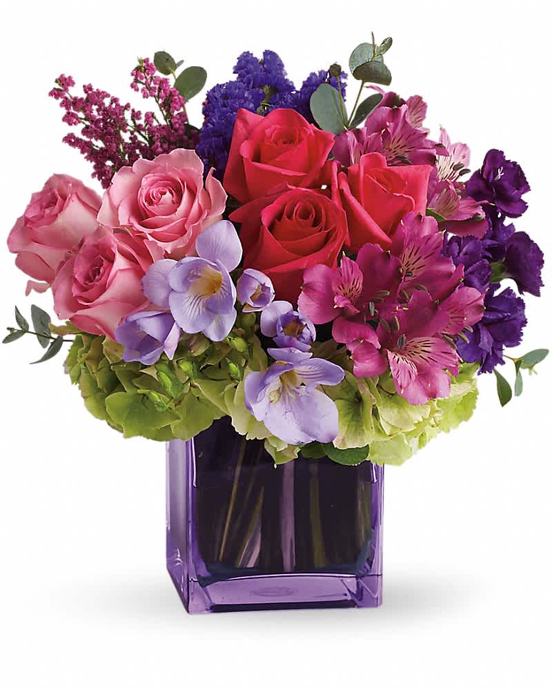 Arrangement of pink roses and purple mixed flowers in a purple glass cube vase