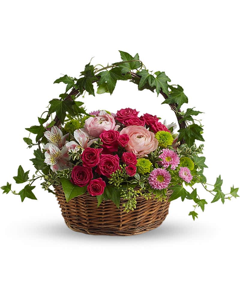 Low wicker basket of pink roses, ranunculus, and mixed blooms with an arching ivy handle