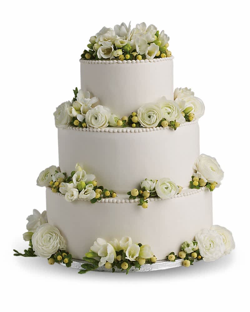 Four-tier white wedding cake decorated with white flowers and green berries around each layer