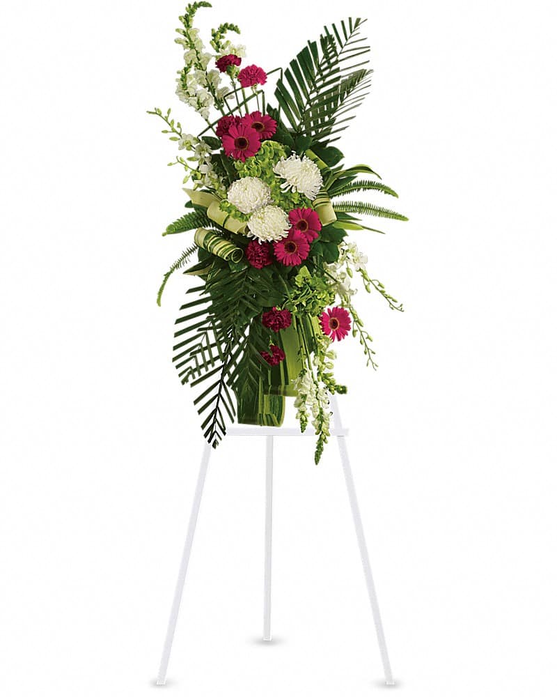 Tall standing spray of hot pink gerberas, white mums, and green blooms with large foliage on a white easel.