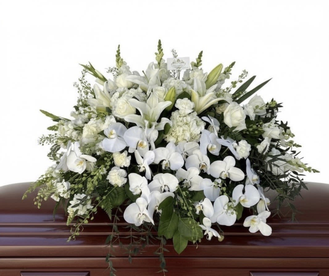 Large white casket spray of lilies, roses, carnations, and orchids on a wooden casket.
