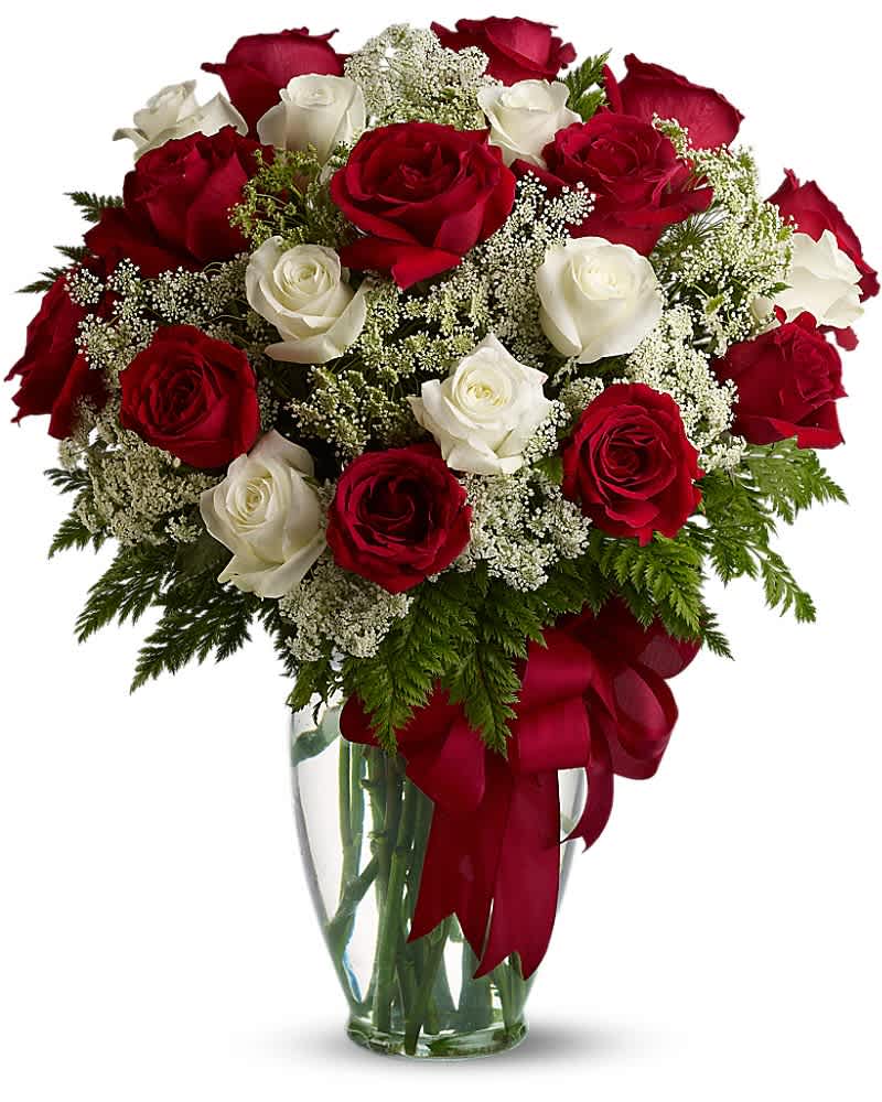 Arrangement of red and white roses with white filler flowers in a clear glass vase with a red bow