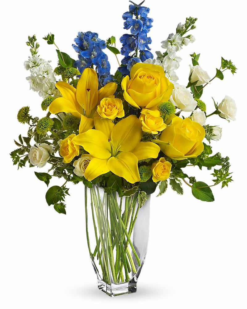 Tall glass vase of yellow lilies and roses with blue delphinium and white blooms