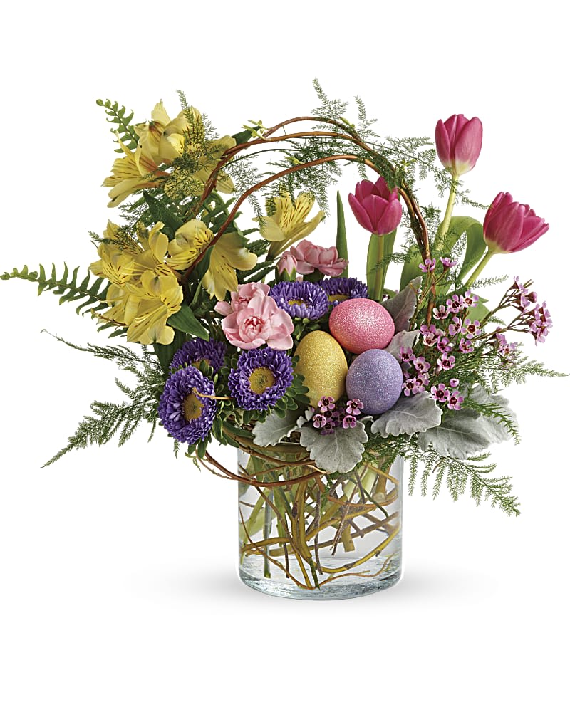 Easter floral arrangement with pink tulips, yellow blooms, purple flowers and pastel eggs in a clear glass vase