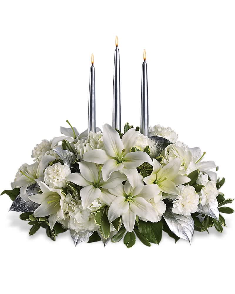 Low centerpiece of white lilies and carnations with silver leaves and three tall silver taper candles