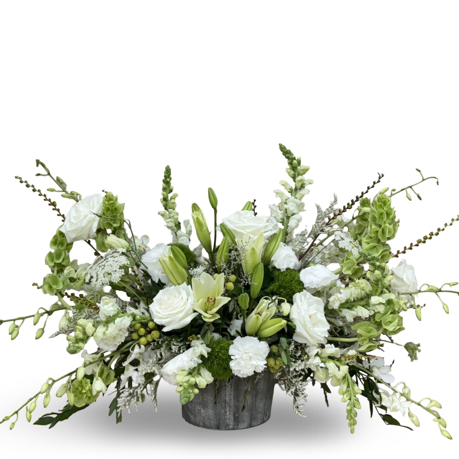 Low white and green arrangement with roses, lilies, and snapdragons in a rustic gray container
