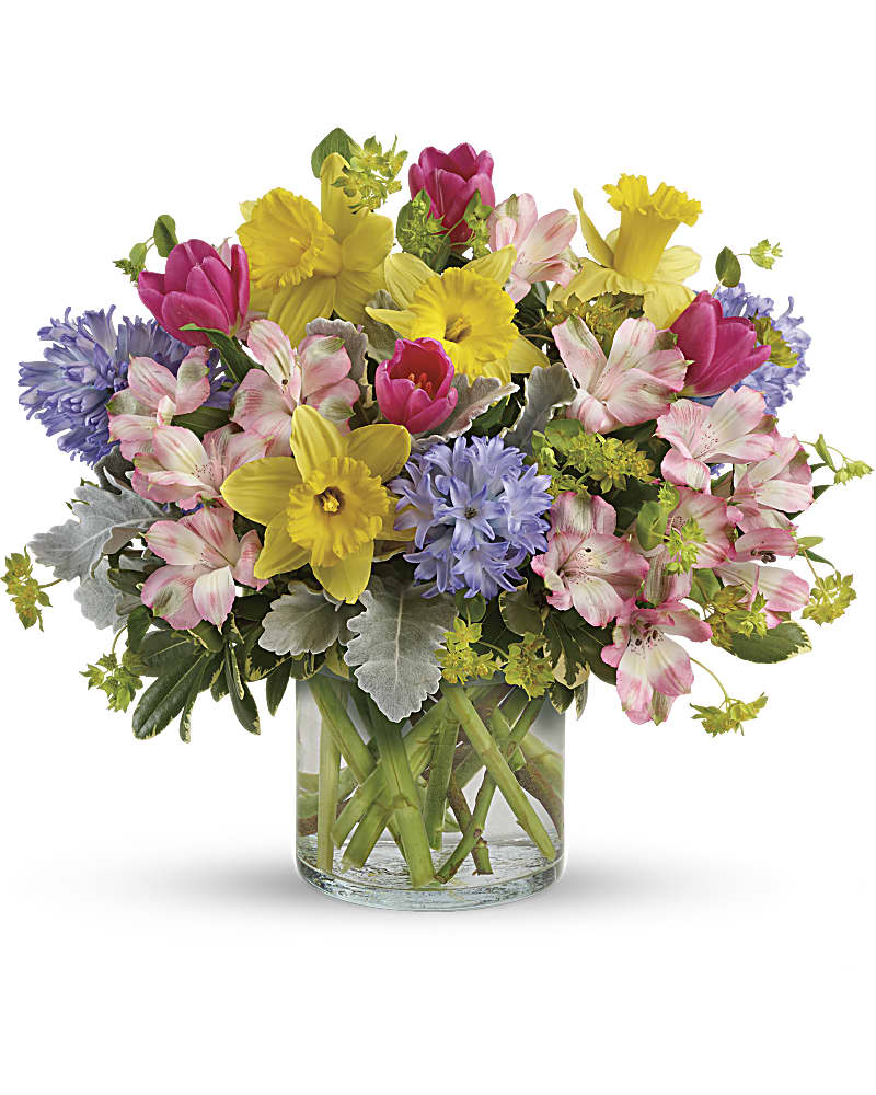 Bright spring bouquet of yellow daffodils, pink tulips, and mixed blooms in a clear glass vase