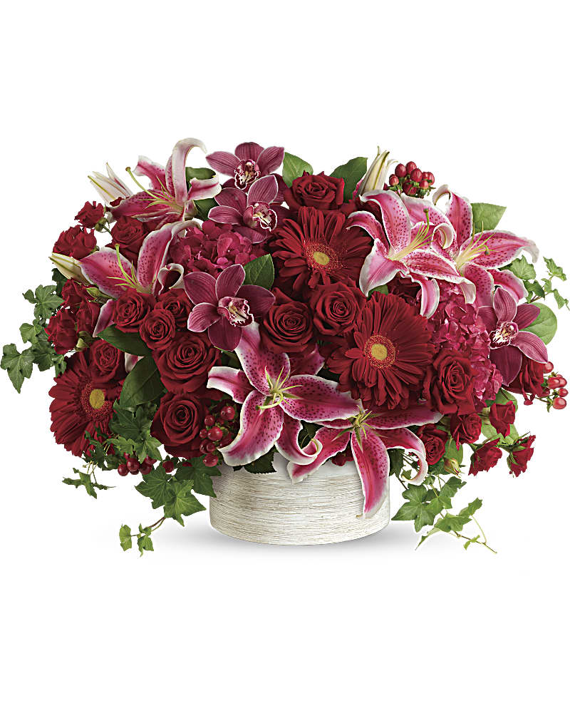 Low arrangement of red and pink flowers with large stargazer lilies in a white ceramic bowl.