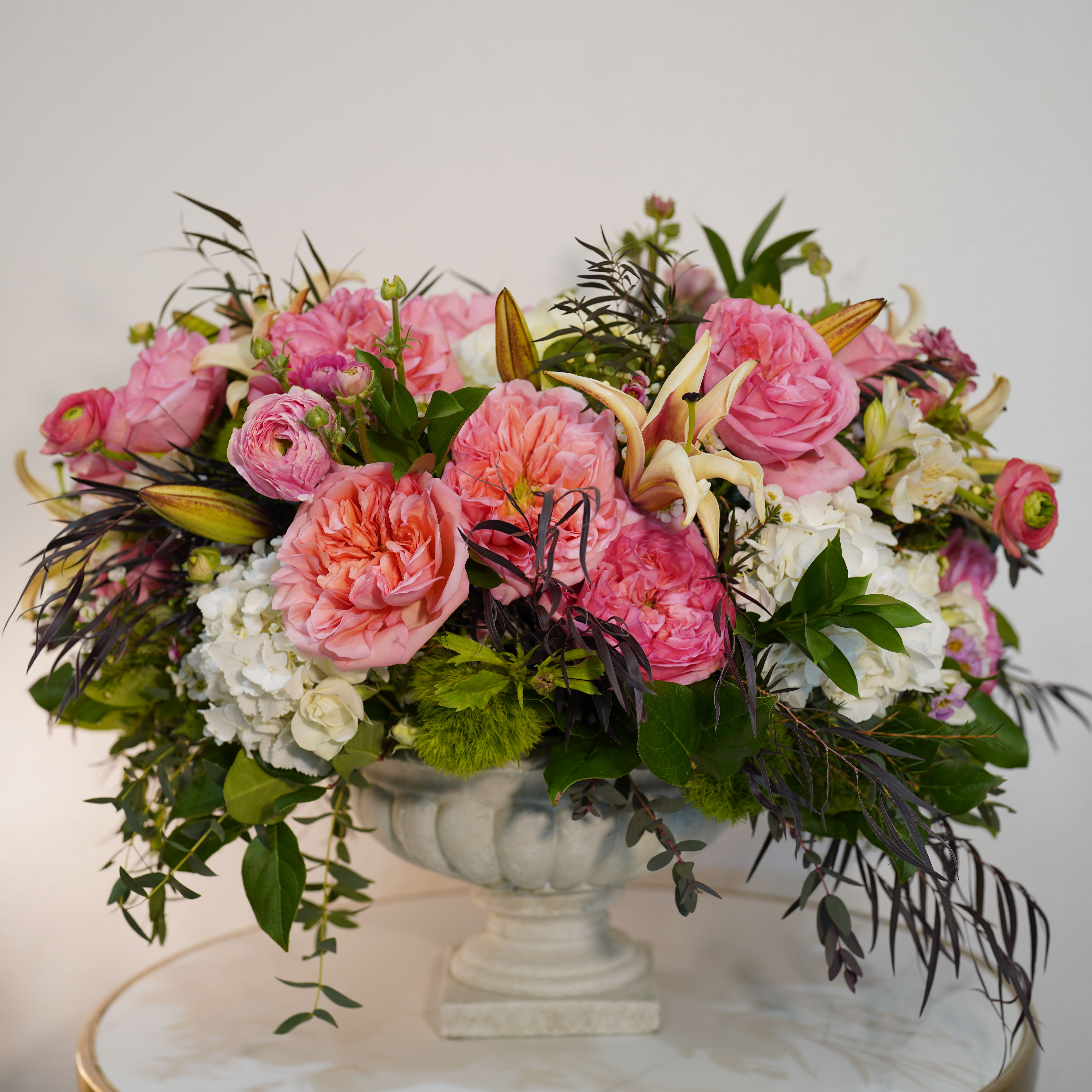 Pink Symphony - Romantic, soft, and full of charm — our Pink Symphony  arrangement is designed to make a lasting impression. This luxurious floral design features premium pink garden roses, delicate ranunculus, seasonal blooms, and lush greenery, all carefully arranged in a classic pedestal vase. The rich textures and soft blush tones create a sophisticated and elegant look that elevates any space. Perfect for anniversaries, birthdays, romantic gestures, or luxury gifting, this arrangement brings beauty, emotion, and style together in one unforgettable piece. Each arrangement is handcrafted by Guy Floral Studio using the freshest flowers available, ensuring a unique and high-end presentation every time. Same-day flower delivery available in Beverly Hills, West Hollywood, Santa Monica, Beverly Grove, Bel Air, Culver City, and surrounding Los Angeles areas. The arrangement shown in the photo reflects our Deluxe size, featuring a fuller, more abundant design with premium blooms.