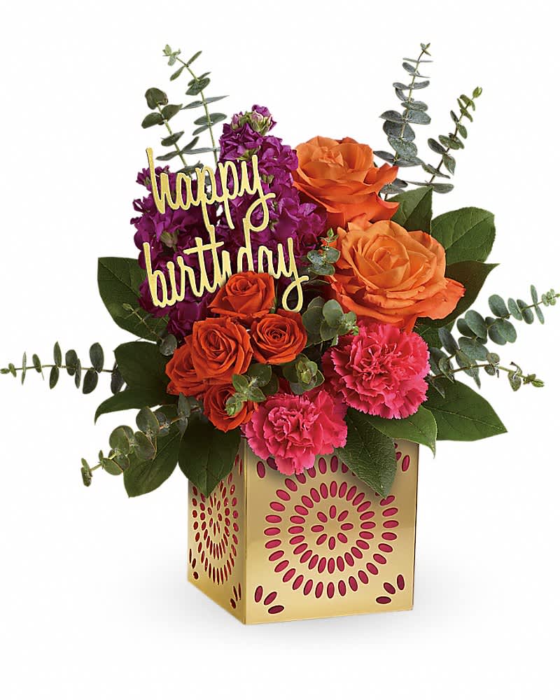 Birthday flower arrangement with orange roses, pink carnations, and purple blooms in a gold cube vase