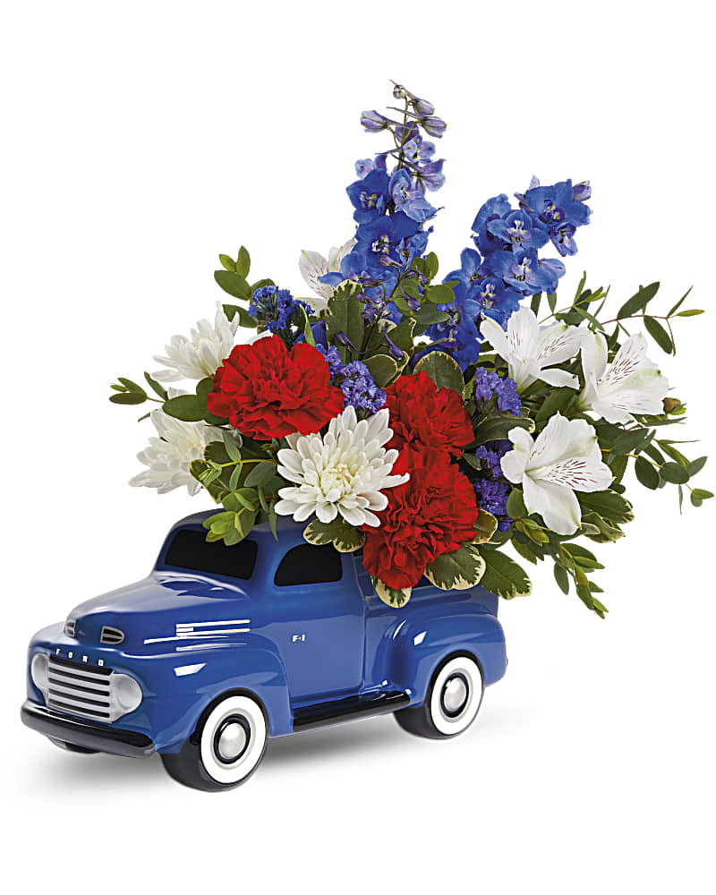 Red, white, and blue flower arrangement in a blue ceramic pickup truck container