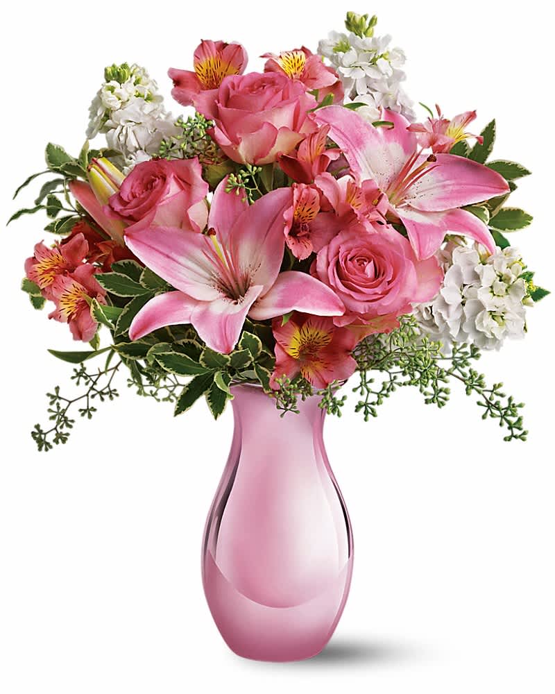 Pink lilies, roses, and white flowers arranged in a pink glass vase