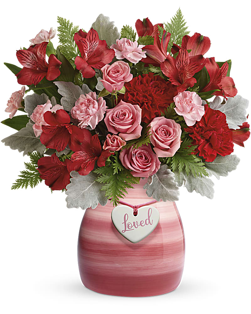 Red and pink roses, carnations, and alstroemeria in a pink vase with a heart tag