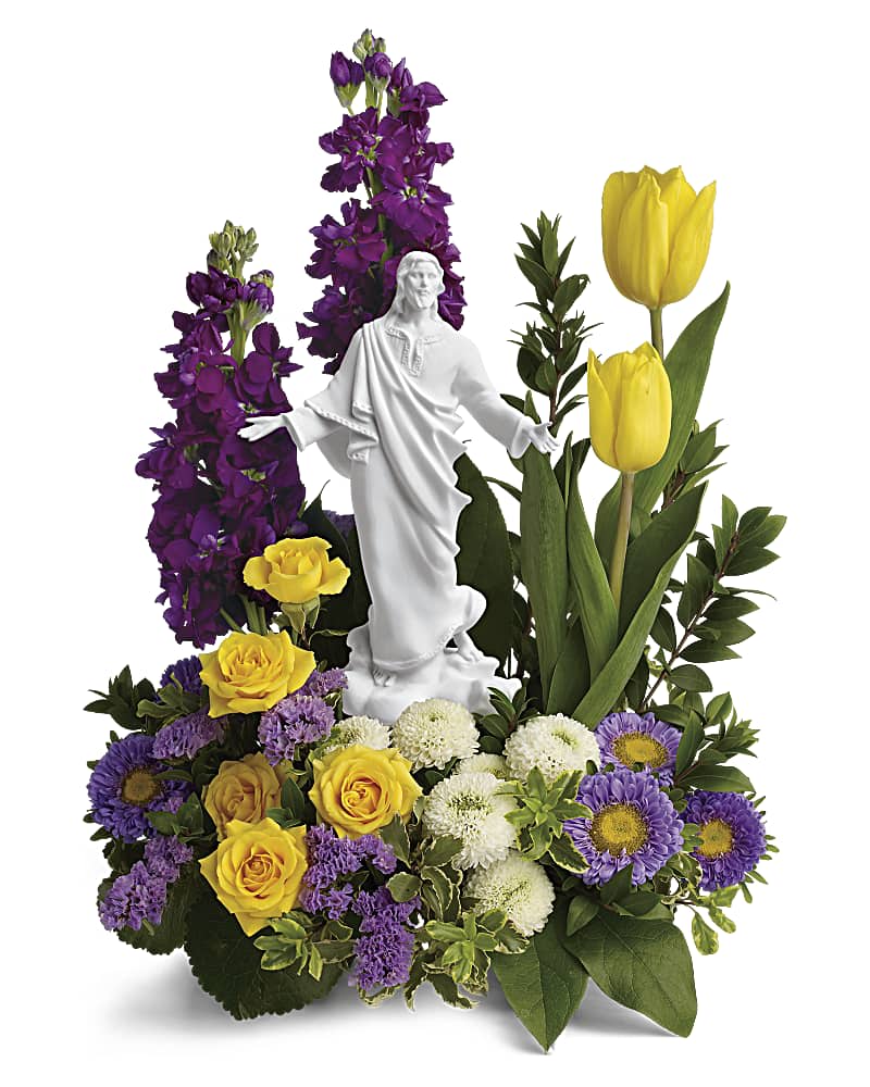 Religious floral arrangement with yellow roses, tulips and purple flowers around a white Jesus figurine