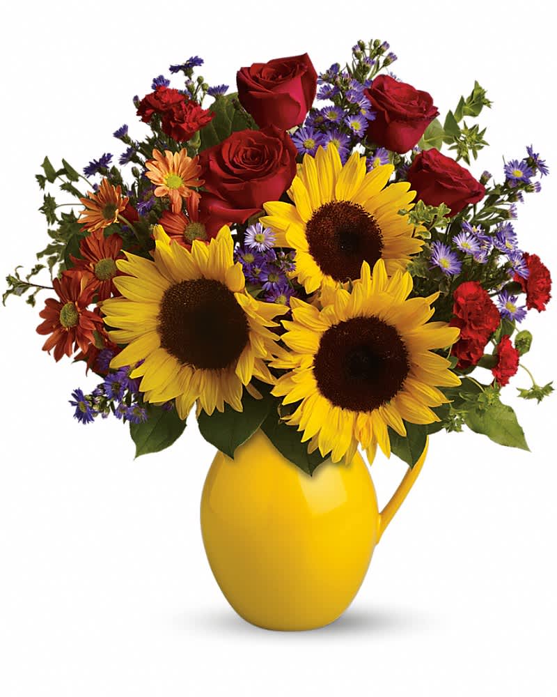 Mixed arrangement of sunflowers, red roses, and fall-toned blooms in a yellow ceramic pitcher