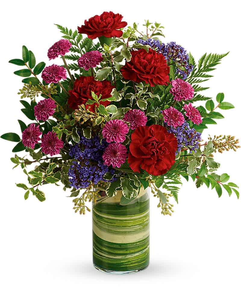 Tall mixed bouquet of red carnations and purple mums in a clear glass vase lined with green leaves