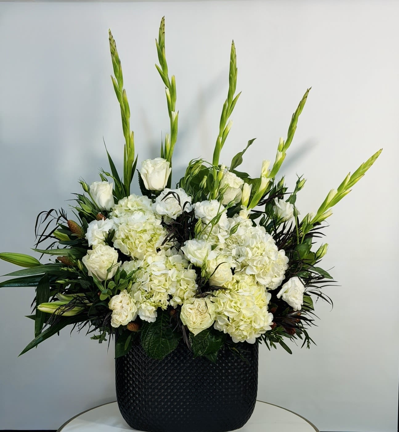 White Noir - A refined and elegant arrangement featuring lush white hydrangea, delicate roses, and fresh seasonal blooms, designed in a modern black textured vase. The contrast between the soft white tones and the bold dark vessel creates a clean, sophisticated, and timeless look. This design brings a sense of calm, purity, and understated luxury perfect for home styling, thoughtful gifts, or elegant occasions. Carefully handcrafted with premium fresh flowers to ensure long lasting beauty and a polished presentation. Same Day Flower Delivery Available across Beverly Hills, Bel-Air, West Hollywood, Beverly Grove, Santa Monica, Culver City, Hollywood Hills, Hollywood, Studio City, Encino, and Sherman Oaks.