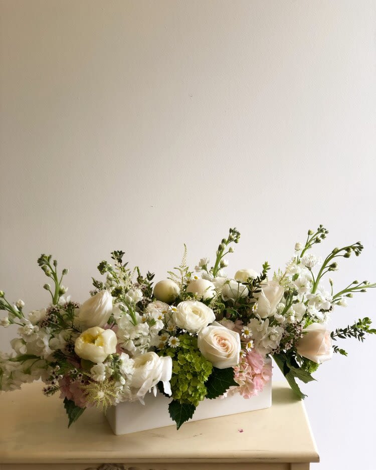 Low centerpiece of white and blush roses with green hydrangea in a white rectangular vase