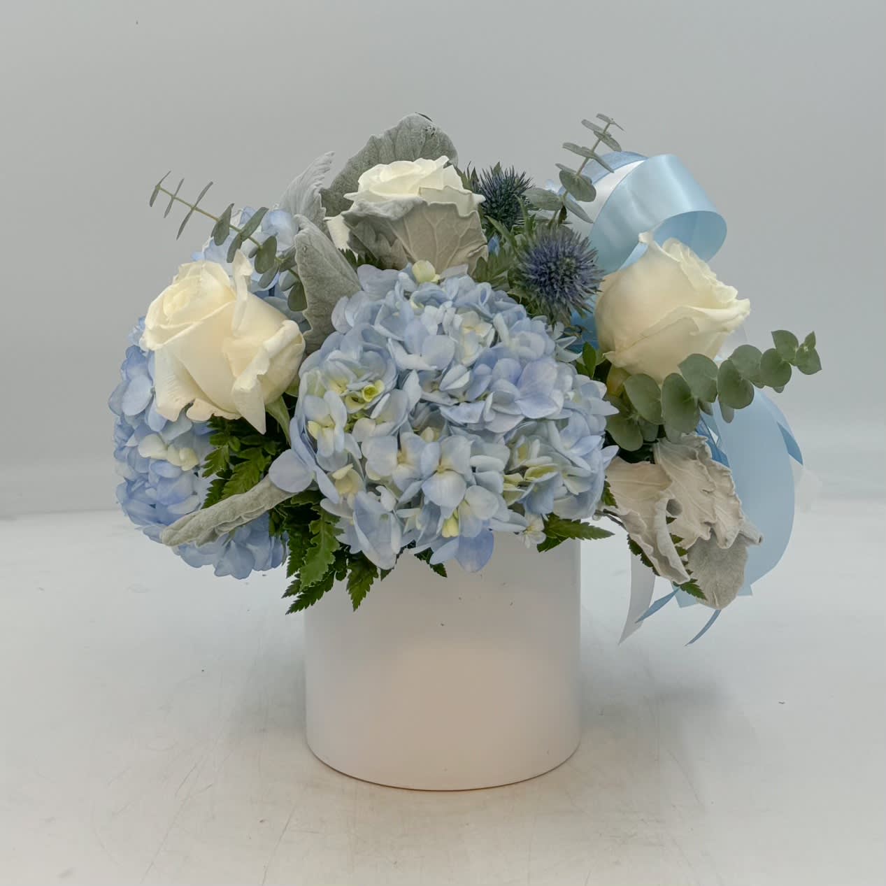 Baby Boy - Baby Boy is an adorable arrangement to celebrate a new bundle of joy that features a Blue Hydrangea, White Roses, Blue Thistle, Dusty Miller and Eucalyptus arranged in a keepsake white ceramic planter and adorned with a baby blue and white bow. 