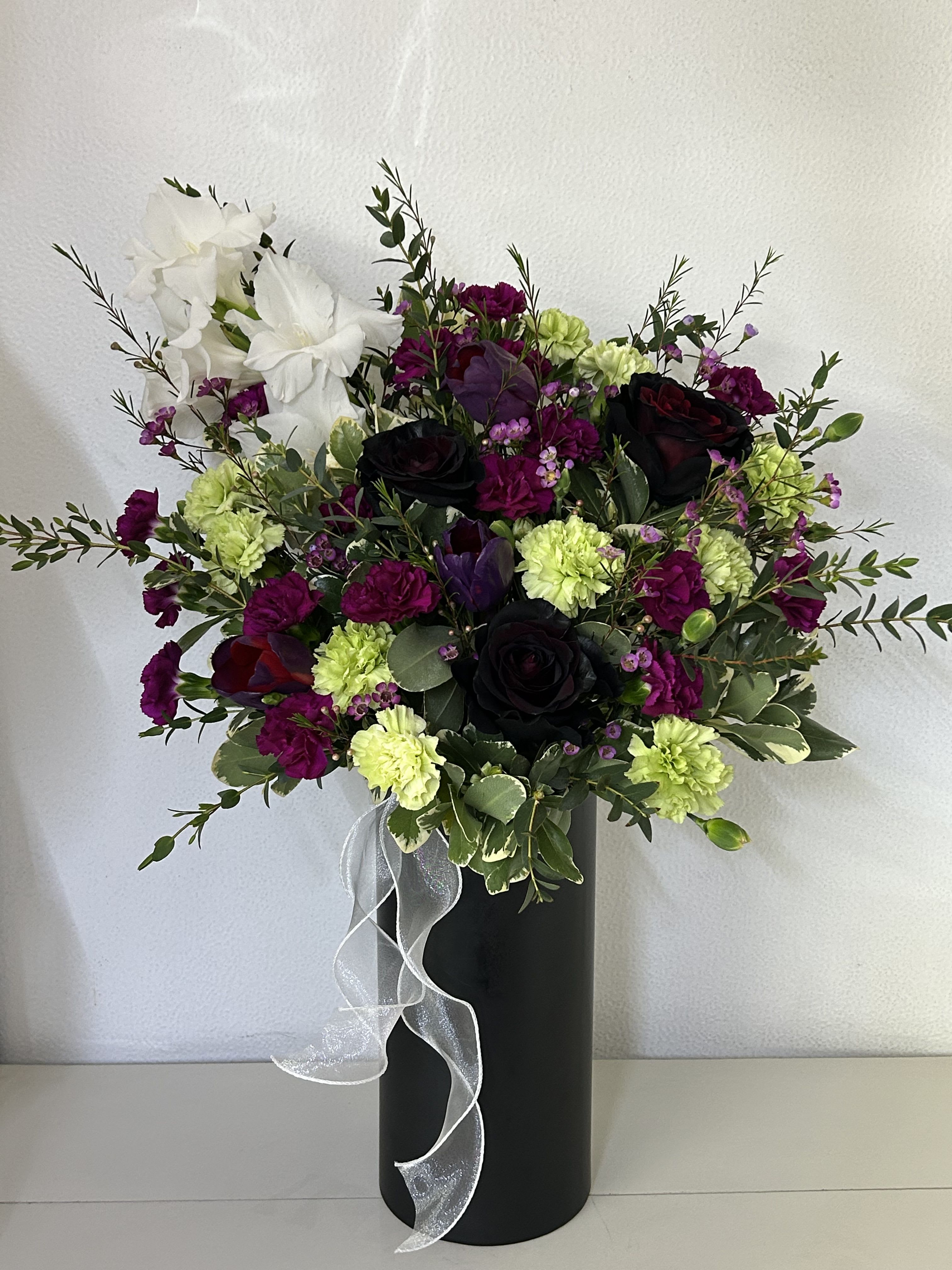 Velvet Blooms - Softly dramatic and effortlessly elegant, Velvet Bloom brings together rich, velvety tones with fresh, natural textures for a look that feels both modern and timeless. Deep hues are beautifully complemented by lighter accents and lush greenery, creating a balanced arrangement with depth and sophistication. Presented in a sleek container with a delicate finishing touch, this design is perfect for any occasion—offering a refined way to express warmth, appreciation, or quiet romance. (If some flowers and/or the vase are not available there will be minor substitutions.)