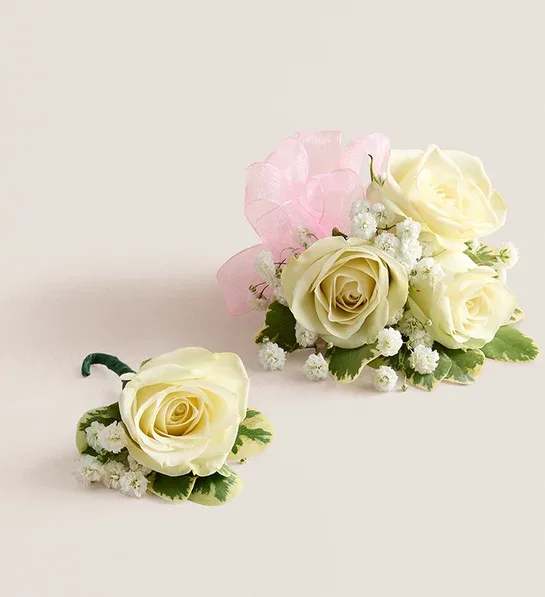 White Spray Rose Corsage &amp; Boutonniere (Pink) - NEW Make a special occasion even more memorable with our hand-designed corsage and boutonniere pairing. Each is made with carefully chosen white spray roses complemented with baby’s-breath and greenery. The corsage, which can be worn on the wrist or pinned to clothing, comes with ribbon in your choice of eight colors: black, gold, green, lavender, light pink, royal blue, silver, or white.