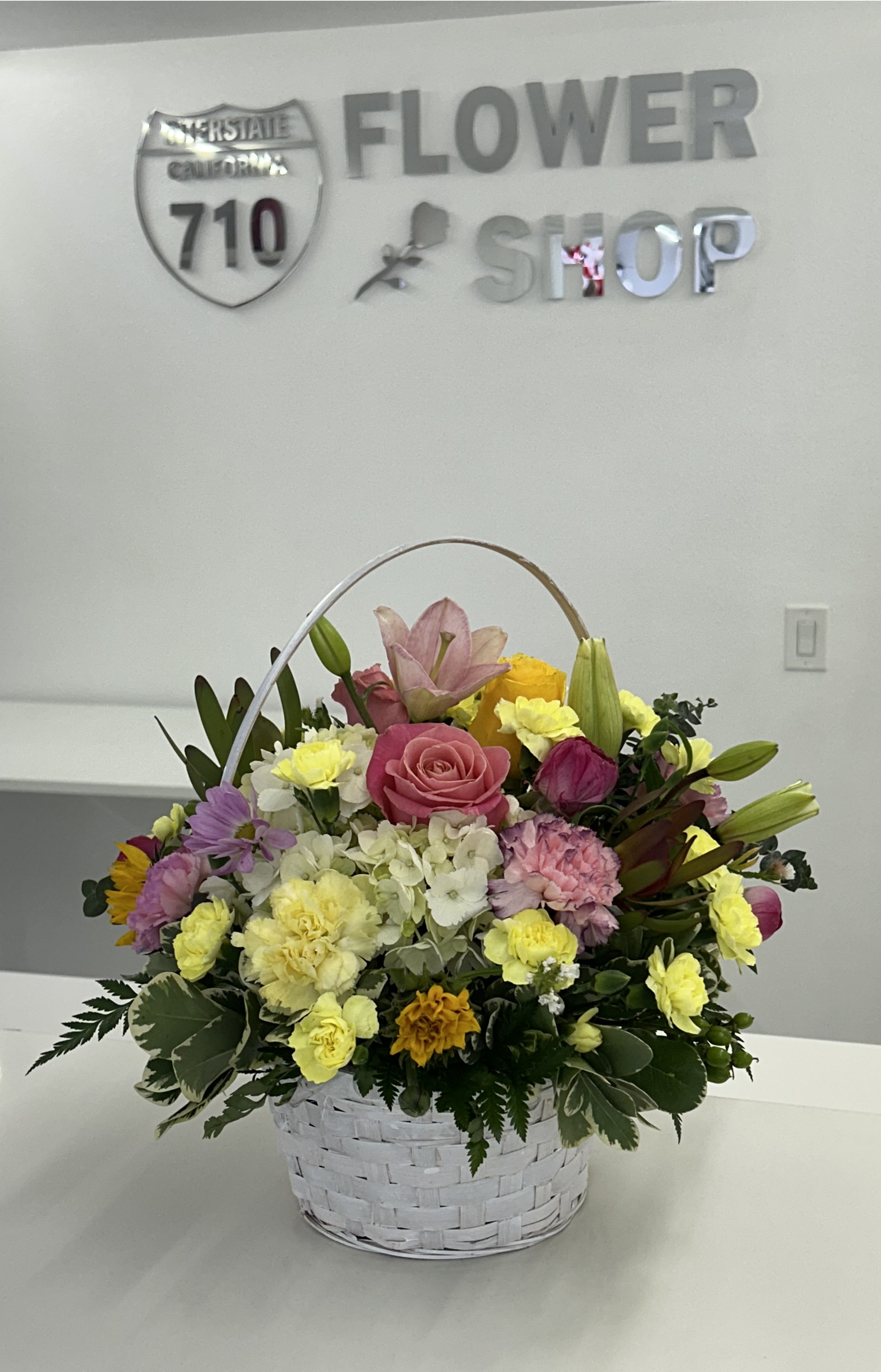 White Garden Basket  - Fresh, soft, and full of charm, White Garden Basket is a beautifully balanced arrangement that captures the essence of a blooming spring garden. Crisp whites are complemented by gentle pinks, cheerful yellows, and touches of soft purple, creating a harmonious blend of color that feels both uplifting and serene. Arranged in a classic white basket, this design brings a light, airy elegance to any setting—perfect for celebrating special moments or simply brightening someone’s day. (If some flowers and/or the vase are not available there will be minor substitutions.)