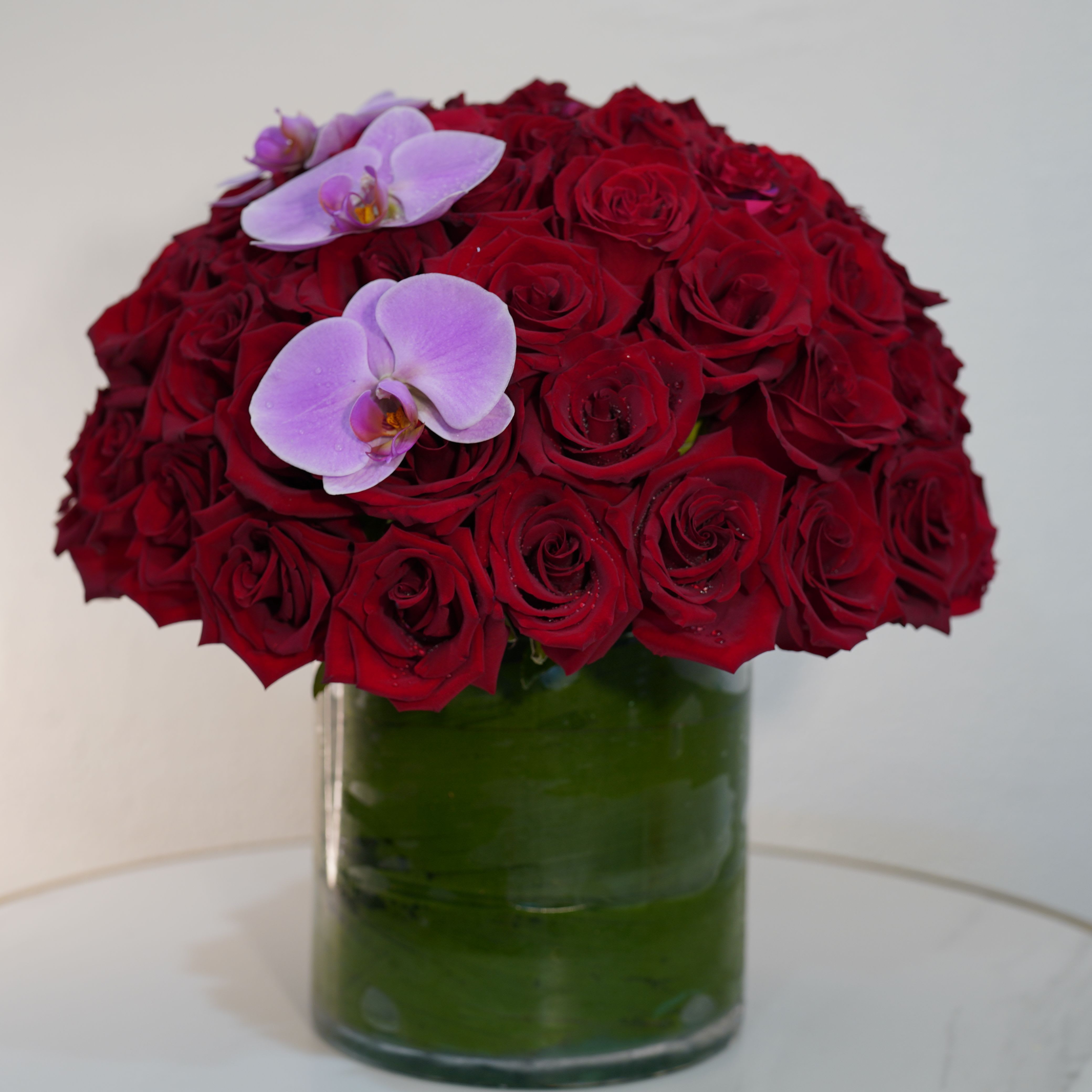 Red Affair  - Bold, romantic, and unforgettable — our Red Affair arrangement is the ultimate expression of love and elegance. Featuring a luxurious dome of premium red roses, accented with delicate white orchids, this design creates a striking contrast that symbolizes passion and sophistication. Arranged in a modern glass vase, this piece delivers a timeless and high-end look. This arrangement is available in three sizes to suit every occasion: Standard includes 50 red roses, Deluxe features 60 red roses, and Premium showcases an abundant 70 red roses for a truly impressive presentation. Perfect for anniversaries, romantic gestures, Valentine’s Day, or when you want to truly impress, this arrangement speaks the language of love without saying a word. Each piece is handcrafted at Guy Floral Studio using the finest fresh roses, ensuring exceptional quality and a stunning presentation. We proudly offer same-day flower delivery in Beverly Hills, West Hollywood, Santa Monica, Beverly Grove, Bel Air, Culver City, Hollywood Hills, and surrounding Los Angeles areas.