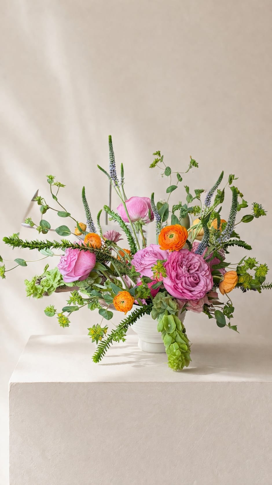 Rainbow Sherbet - Rainbow Sherbet blends lush pink garden roses with vibrant pops of coral ranunculus, layered among airy veronica and fresh seasonal greens.  The arrangement unfolds with a natural, airy movement—each stem reaching outward to create a sculptural, garden-gathered feel. Bright citrus tones mingle with delicate blush, evoking that sweet, sunlit moment of summer in full bloom.  Cheerful, textural, and effortlessly elevated, this piece brings a fresh burst of color and modern charm to any setting.