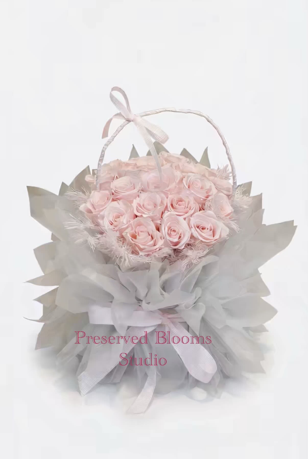 Round basket of pale pink roses wrapped in soft gray tulle with a ribbon handle