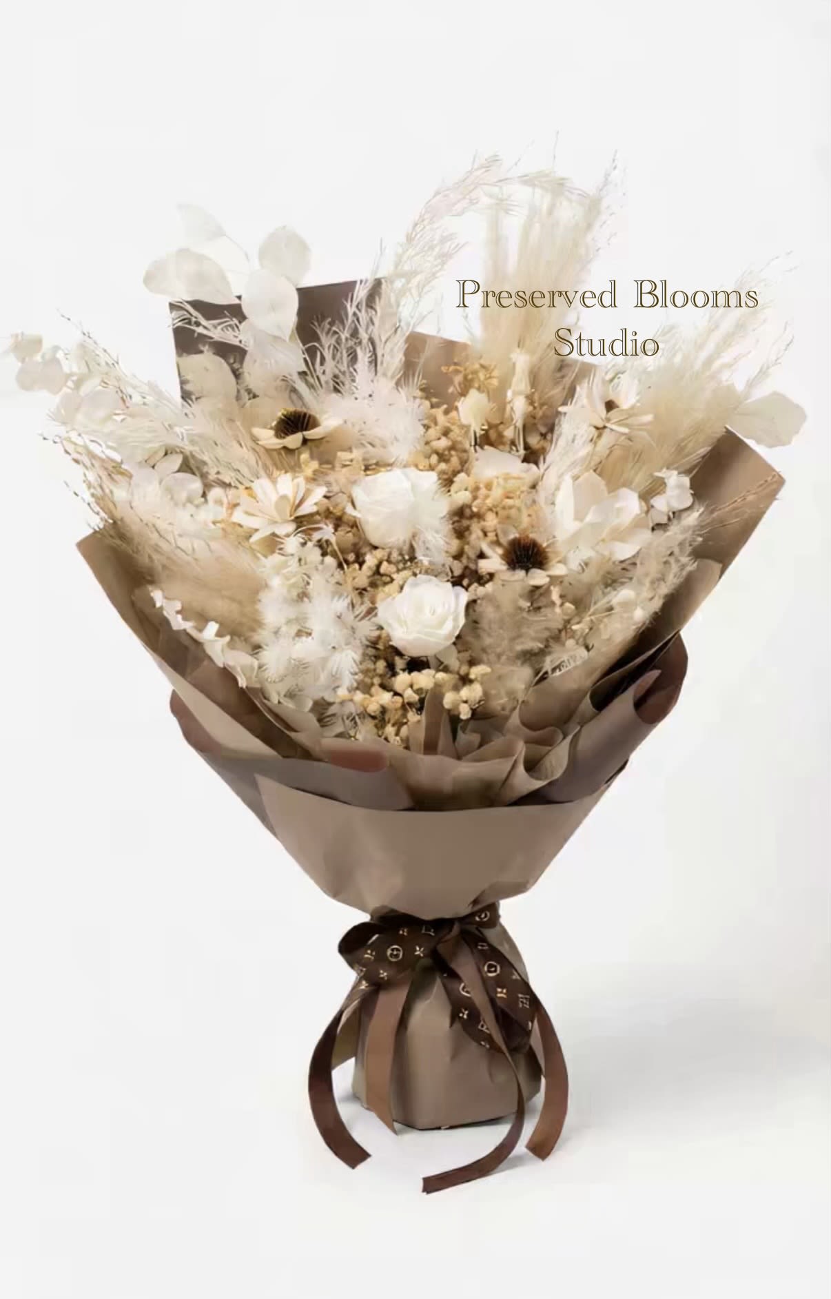 Neutral-toned bouquet of preserved white roses and dried flowers wrapped in brown paper with a dark ribbon.