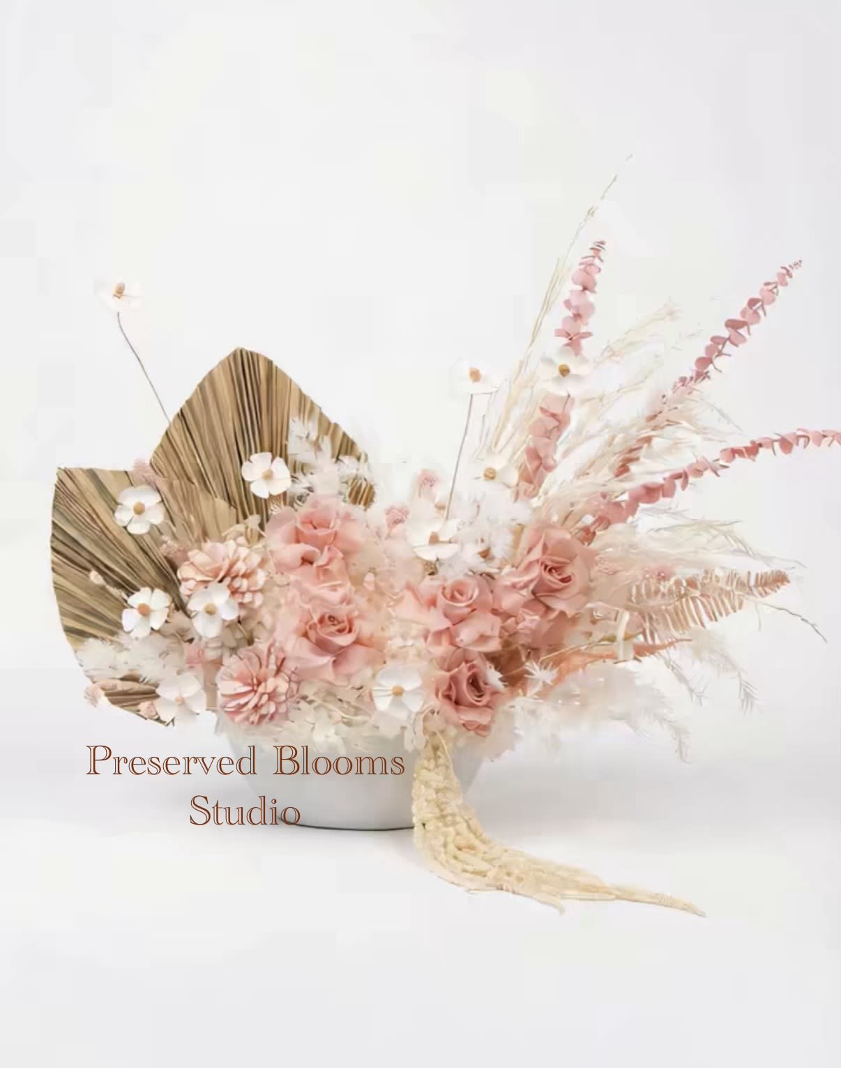 Low arrangement of blush roses, white daisy-like flowers, and dried accents in a white bowl.
