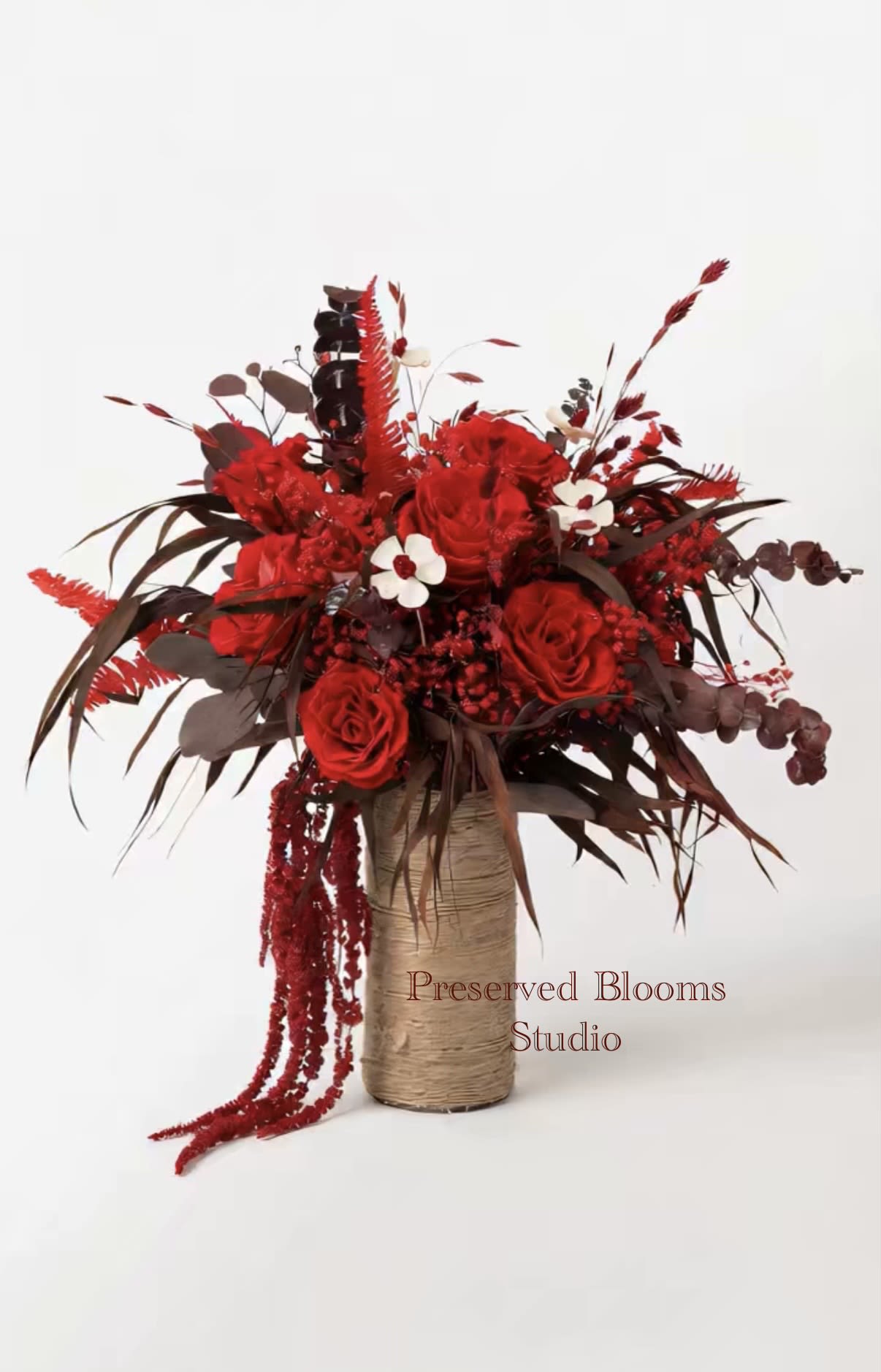 Tall arrangement of deep red roses and berries in a twine-wrapped cylinder vase