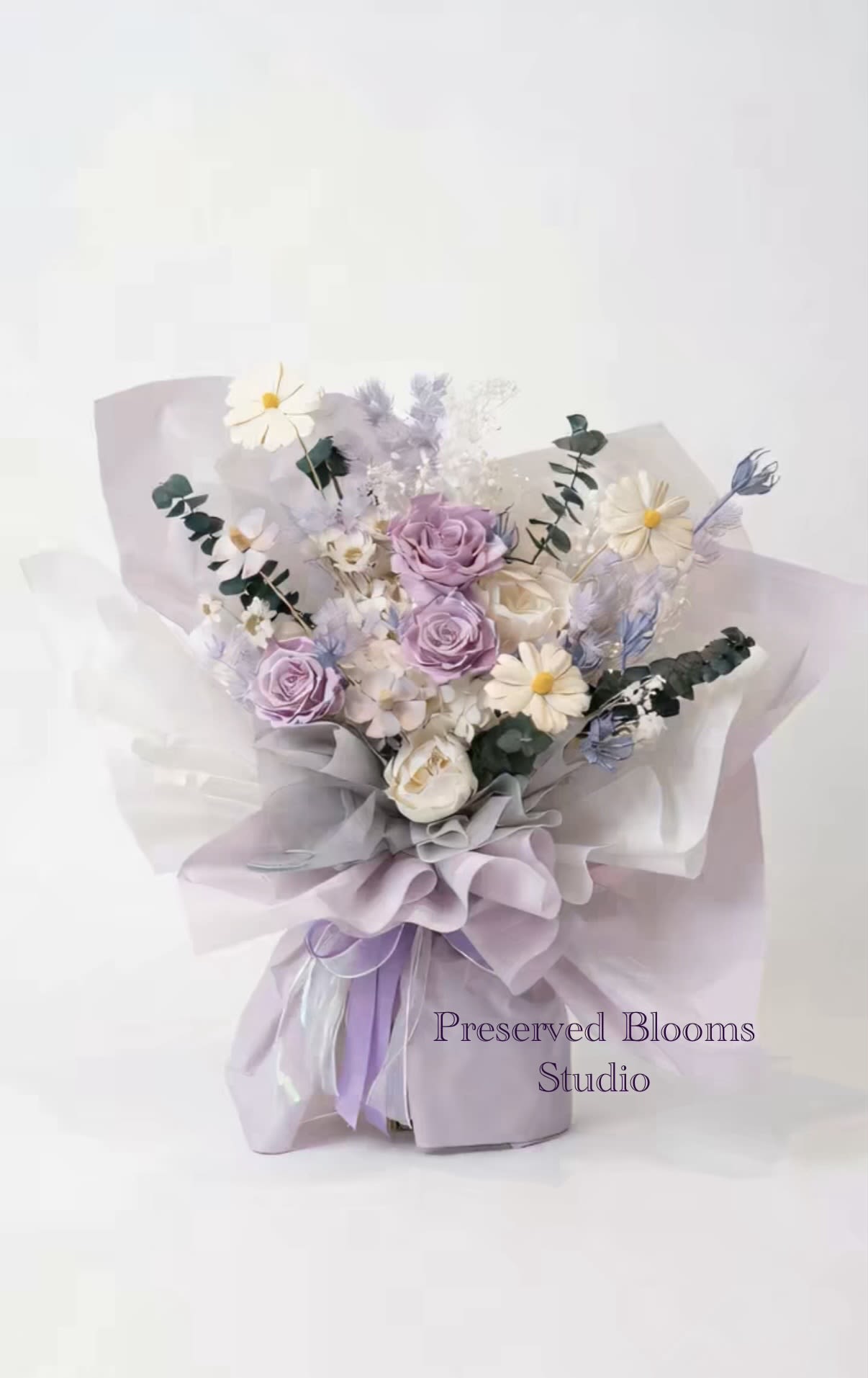 Hand-tied bouquet of lavender roses and white daisies wrapped in layered lilac and white paper.