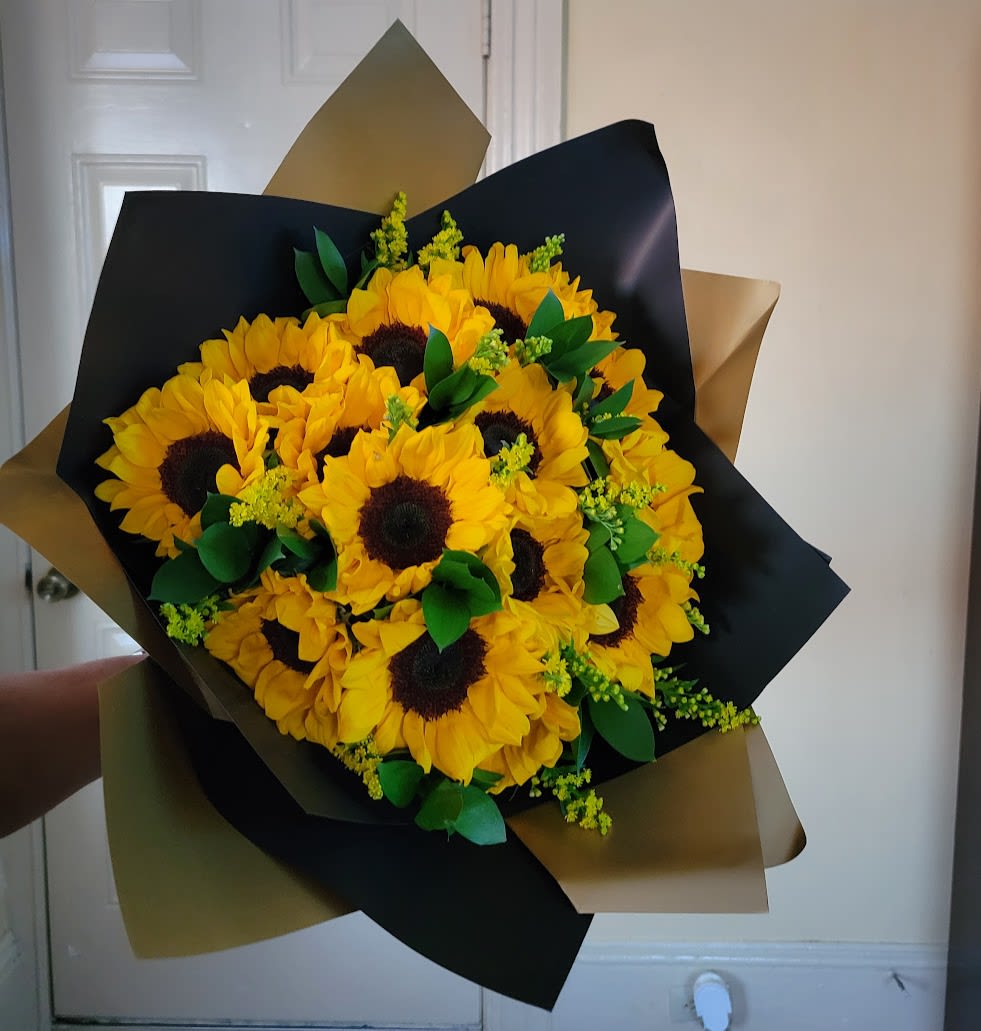 Hand-tied bouquet of bright yellow sunflowers wrapped in black and gold paper.