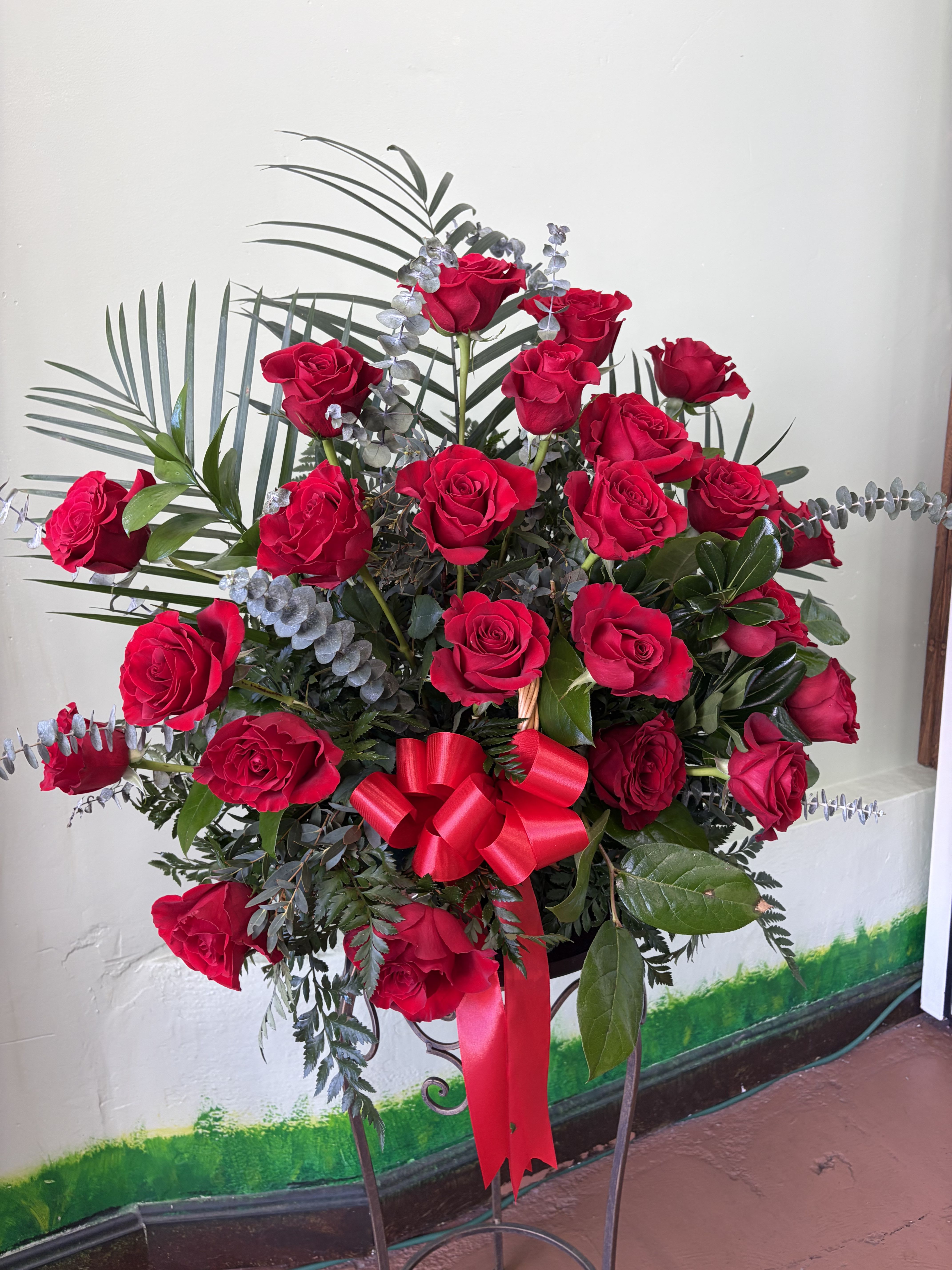 Red Remembrance  - A graceful one-sided arrangement of rich red roses, thoughtfully designed to express love, respect, and heartfelt sympathy. Accented with lush greenery and soft eucalyptus, and finished with a flowing red ribbon.