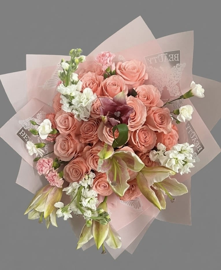 Hand-tied bouquet of peach roses, white blooms, and lilies wrapped in pink paper
