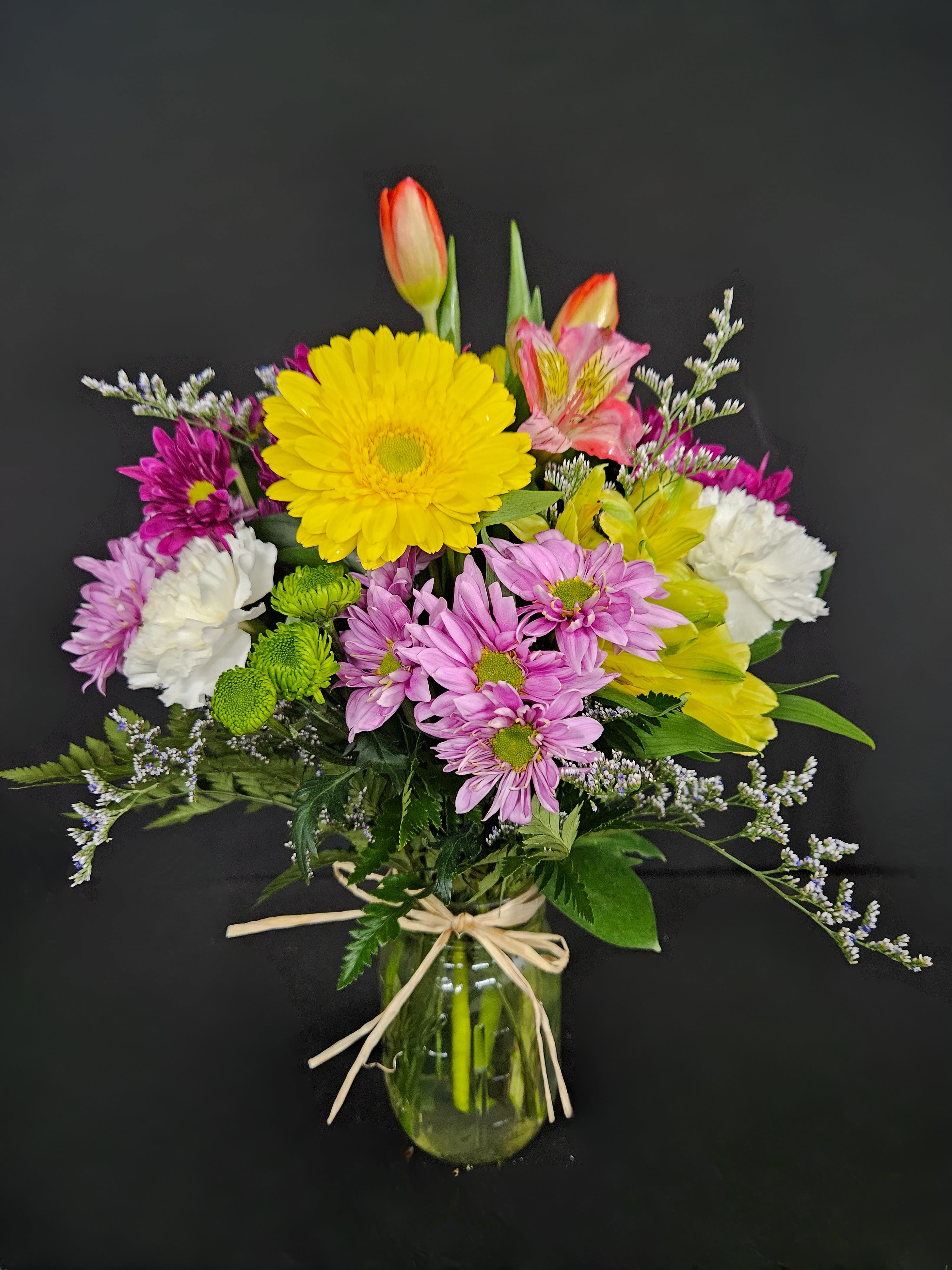 Mixed spring bouquet with yellow gerbera, tulips, carnations and daisies in a glass jar vase.