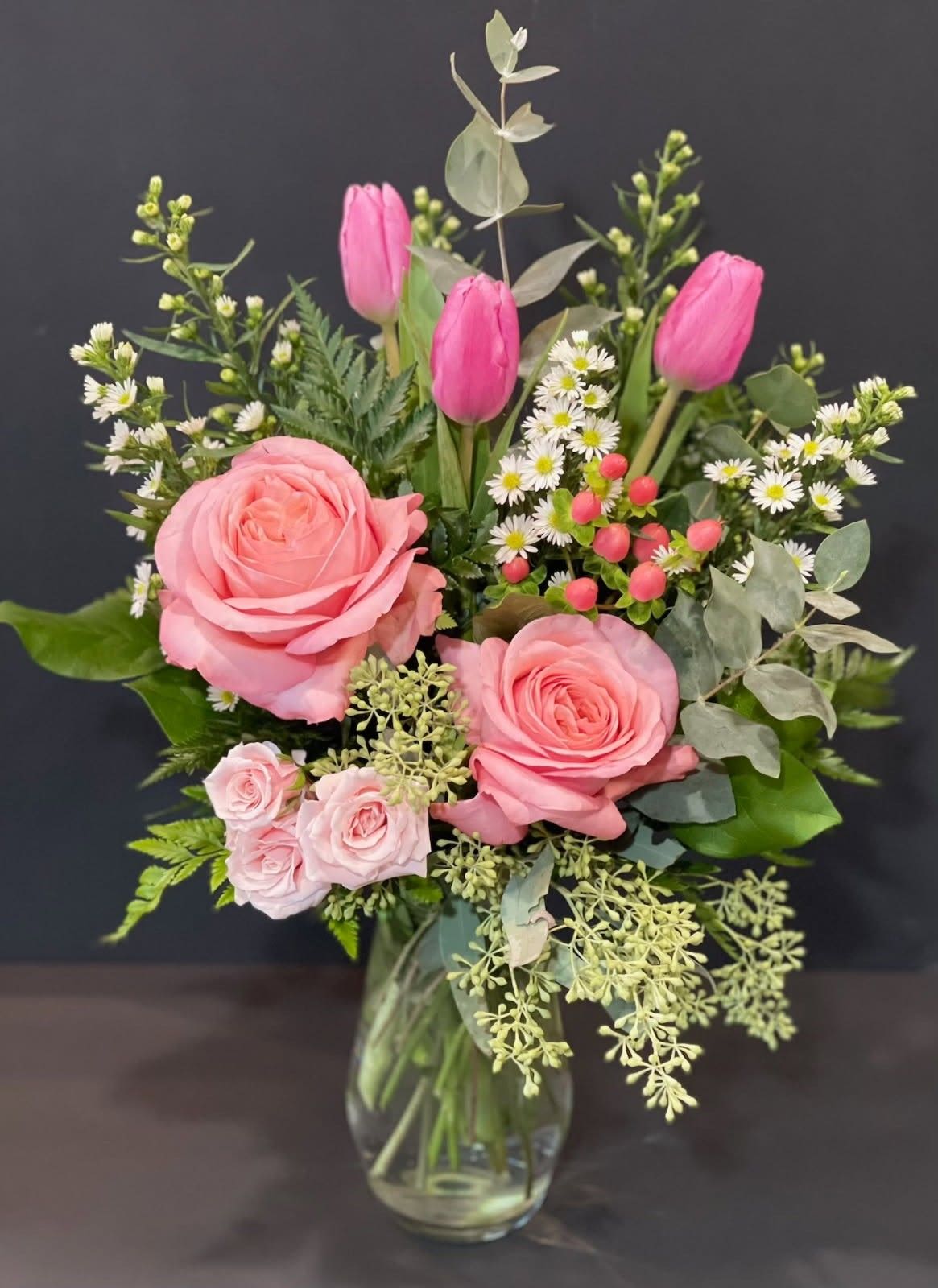 Sweet Blossom Garden - A cheerful mix of soft pink roses, tulips, spray roses, dainty white wildflowers, and fresh greenery arranged in a classic glass vase. Accented with delicate berries and silvery eucalyptus, this design has a fresh-from-the-garden feel that is perfect for birthdays, new babies, anniversaries, or simply brightening someone’s day.  Please note: Due to seasonal and supplier availability, some flowers or accents may be substituted with blooms of equal or greater value while maintaining the same overall style, color palette, and beauty of the arrangement.