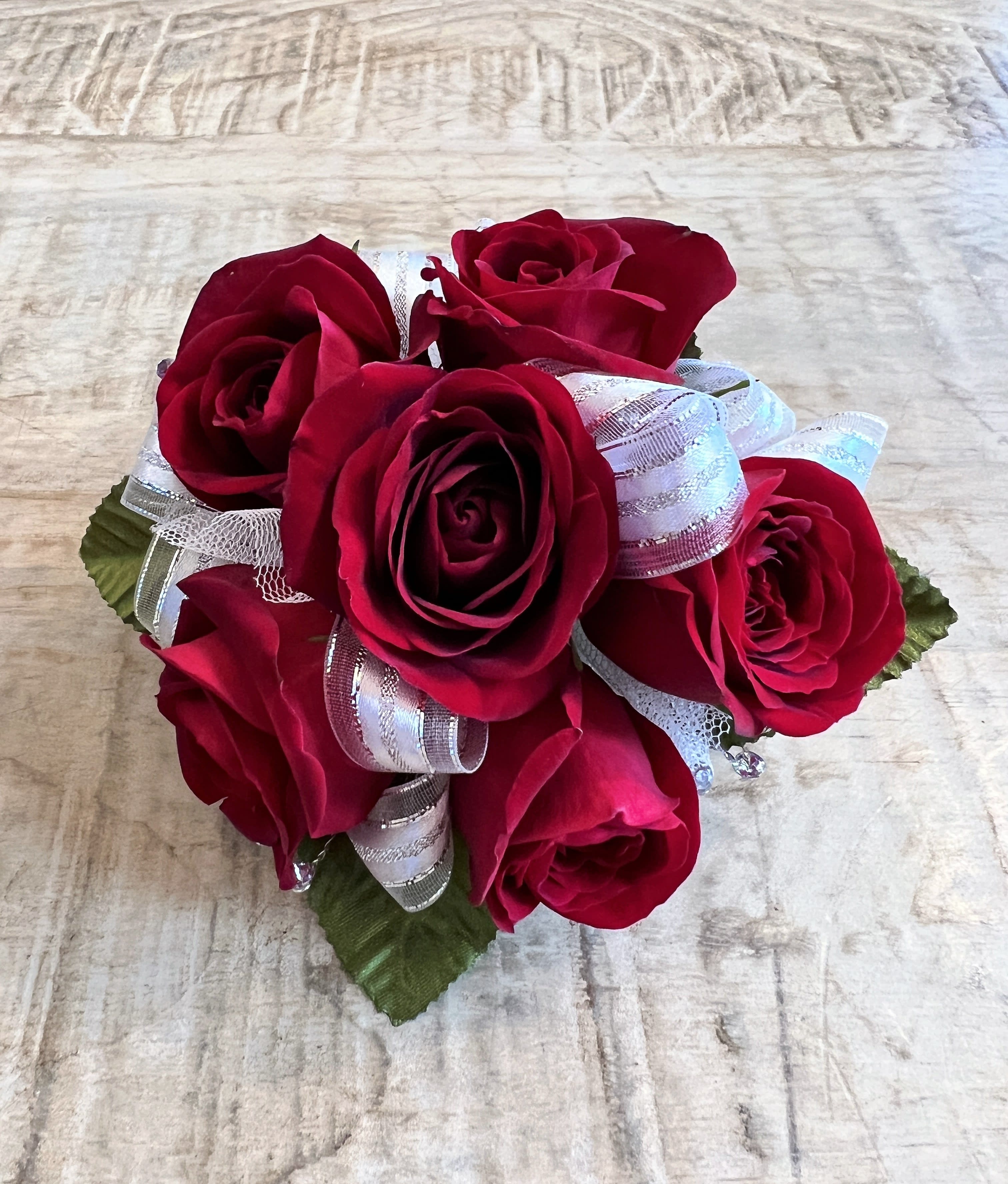 Compact cluster of red roses with silver and white ribbon in a round posy on a light wood surface