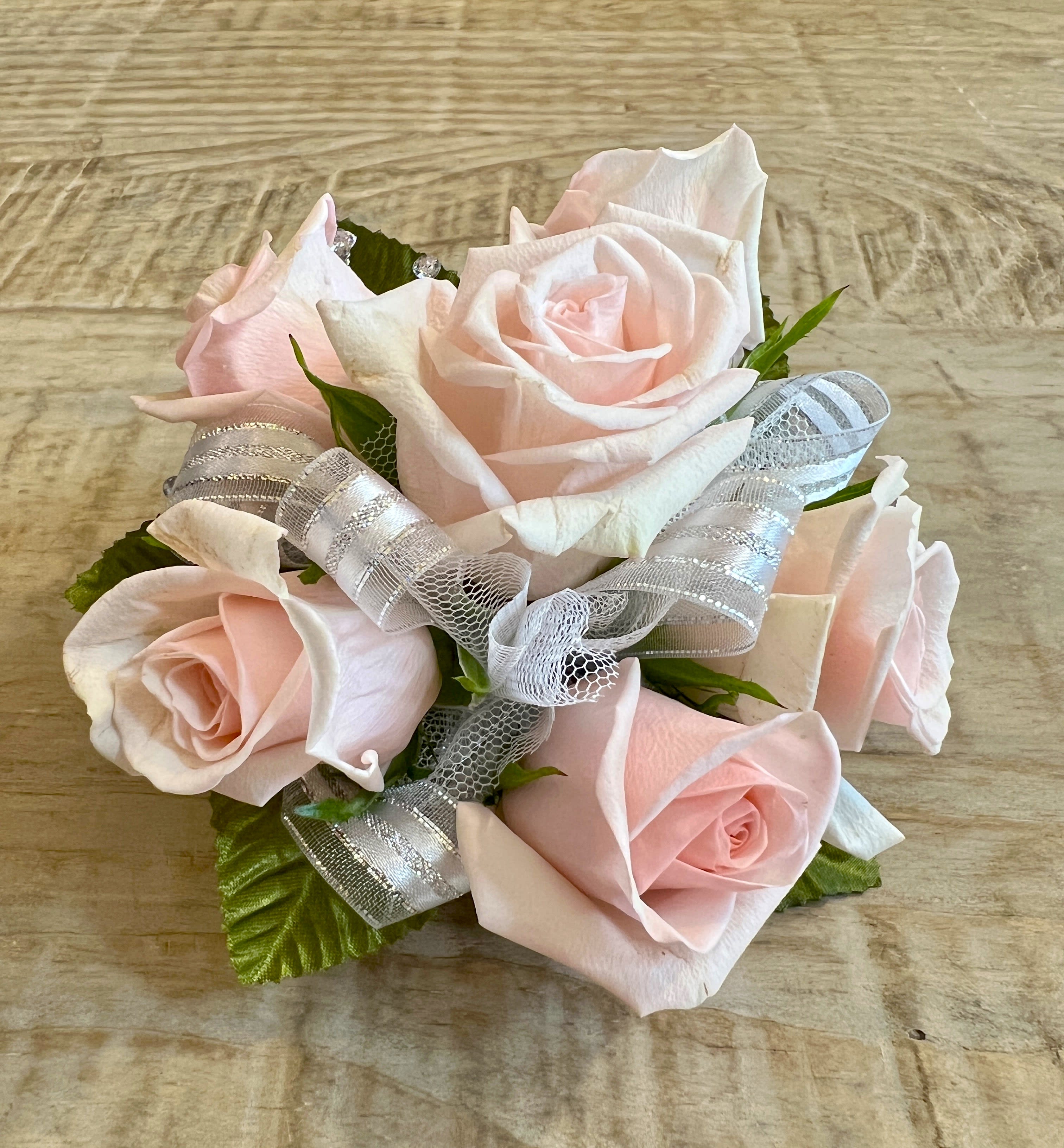 Small cluster of pale pink roses accented with silver and white ribbon on a wood surface
