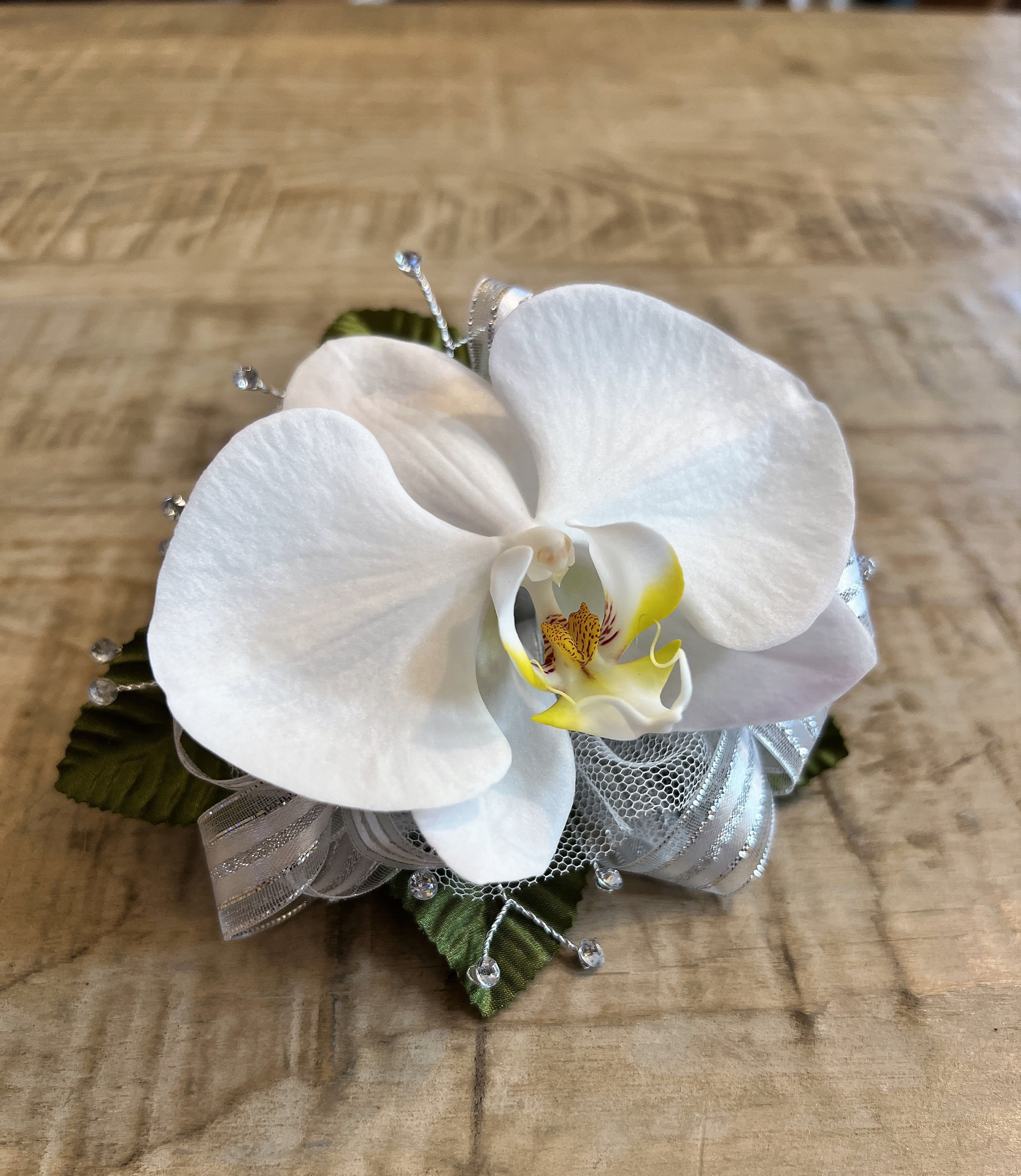 White orchid corsage with silver ribbon and bead accents on a wooden surface