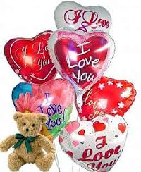 Cluster of heart-shaped I Love You balloons with a small tan teddy bear with green ribbon