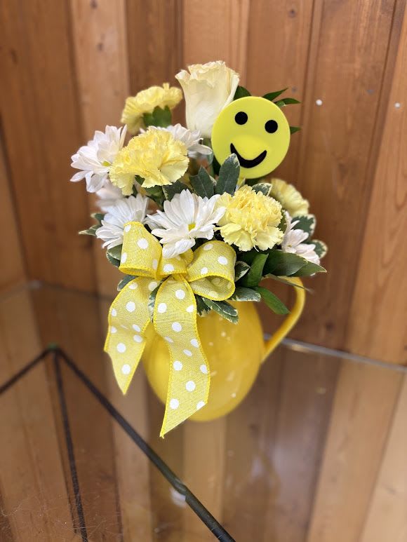 Sunshine Smiles Bouquet - Brighten someone’s day with our cheerful Sunshine Smiles Bouquet! Designed in a vibrant yellow ceramic pitcher, this arrangement features soft white daisies, sunny yellow carnations, and a creamy white rose, accented with fresh greenery. A playful smiley face pick and a yellow polka dot bow add a fun, uplifting touch—perfect for get well wishes, birthdays, or just because. This happy little arrangement is guaranteed to deliver smiles!