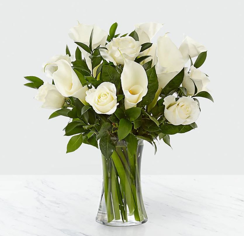 Arrangement of white roses and white calla lilies in a clear glass vase