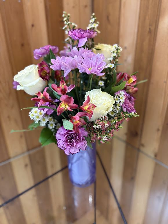 Painted Petals - Painted Petals is a beautifully artistic arrangement bursting with soft color and texture. Designed in a sleek lavender vase, this bouquet features delicate pink daisies, creamy white roses, vibrant alstroemeria, and ruffled carnations, all accented with airy filler flowers and fresh greenery. The blend of blush, berry, and ivory tones creates a hand-painted look that feels both elegant and whimsical—perfect for birthdays, celebrations, or simply brightening someone’s day with a touch of floral artistry.