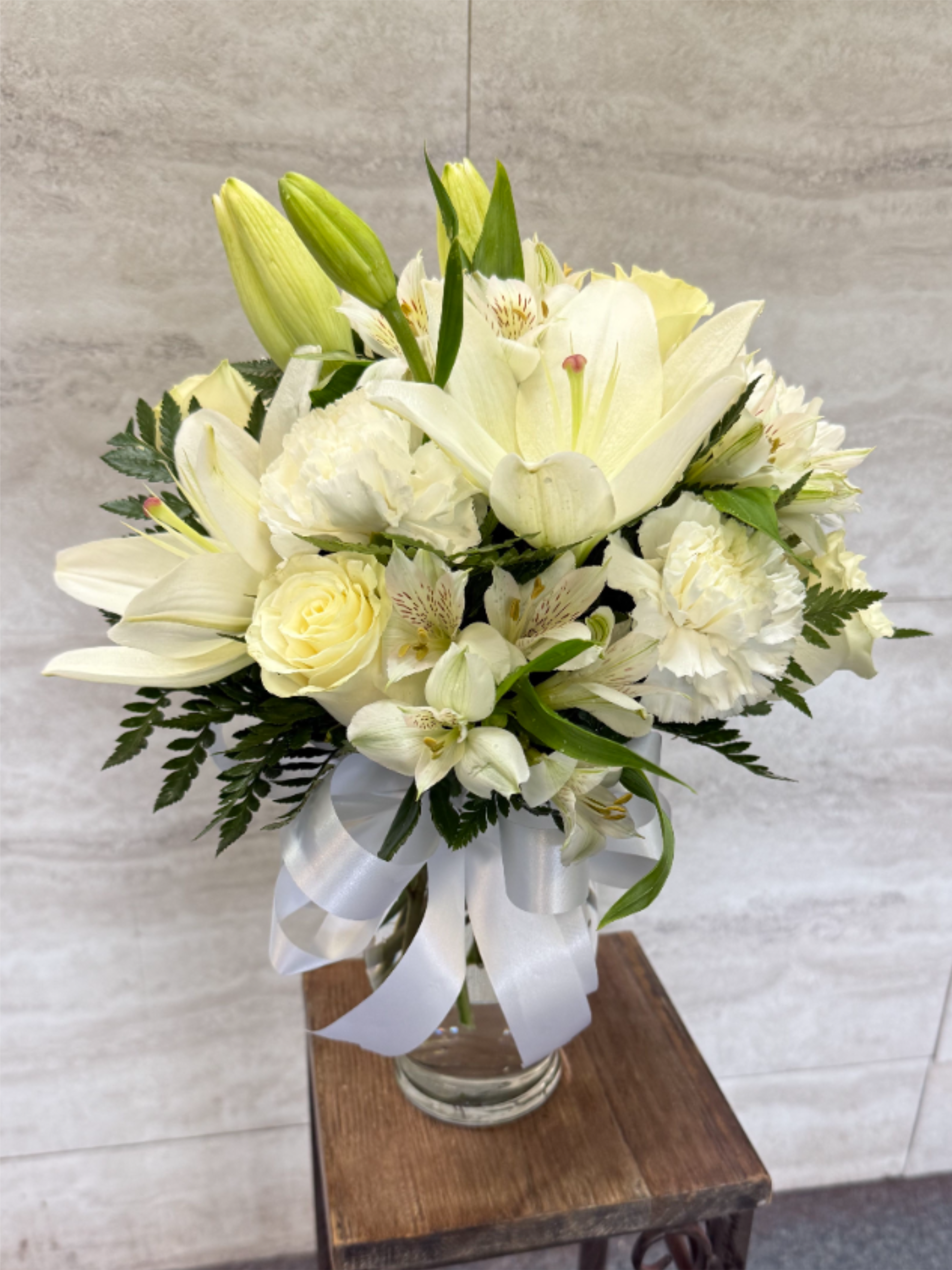 White Aura - **White Aura**   A dreamy all-white bouquet featuring elegant roses, soft cushions, and graceful lilies, beautifully wrapped with a delicate white bow. Its pure tones create a clean, timeless look that feels both luxurious and serene—perfect for any moment that calls for simple elegance. 